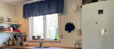 Una cocina con ventana, pileta, alacenas y refrigerador.