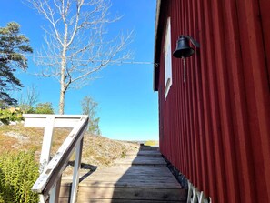 A wooden deck leading to a red building with a bell on the side. - 4 Star Holiday Home in Trollhattan (Trollhattan)