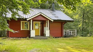 A small, single-story wooden cabin with a yellow door and windows, surrounded by a grassy yard and trees. - 4 Person Holiday Home in Hjarnarp (Hjarnarp)