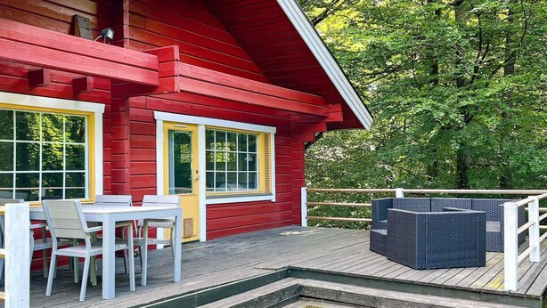 A red wooden building with a deck, white outdoor furniture, and a small garden area. - 4 Person Holiday Home in Hjarnarp (Hjarnarp)
