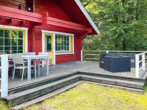 A red wooden building with a deck, white outdoor furniture, and a small garden area. - 4 Person Holiday Home in Hjarnarp (Hjarnarp)