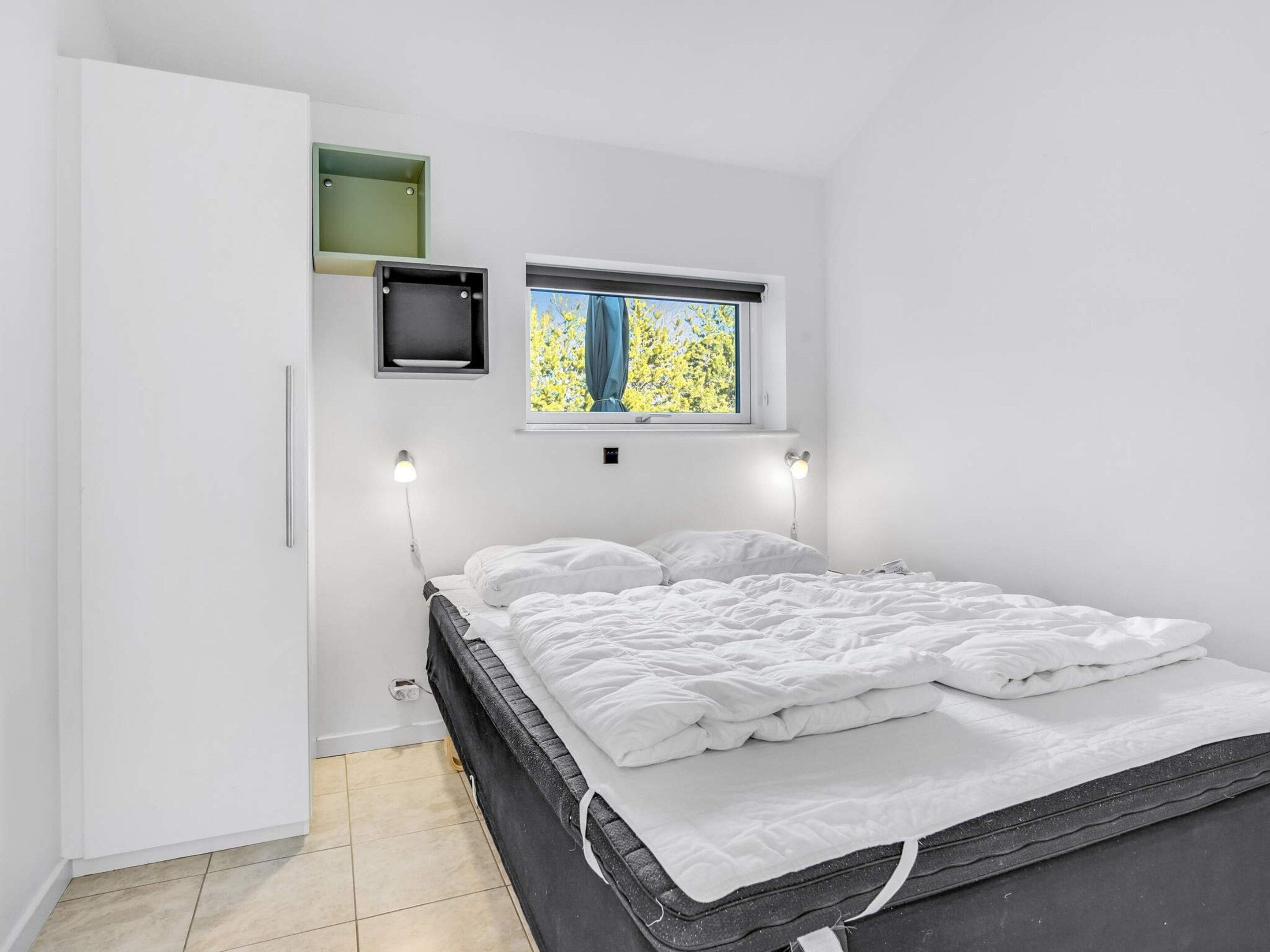 A bedroom with a bed, a window with a view of trees, a wall-mounted TV, and a wardrobe.