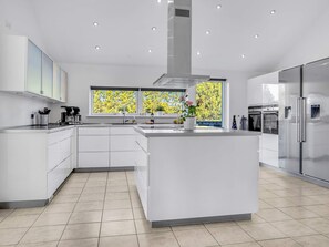 A modern kitchen with white cabinetry, a central island, a large window with a view of trees, and built-in appliances.