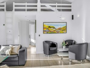 A modern living room with a sofa, two armchairs, a coffee table, and a painting on the wall.