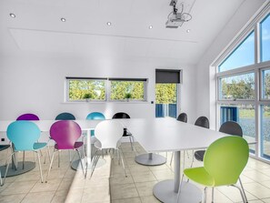 A conference room with a white table and colorful chairs, large windows, and a projector.