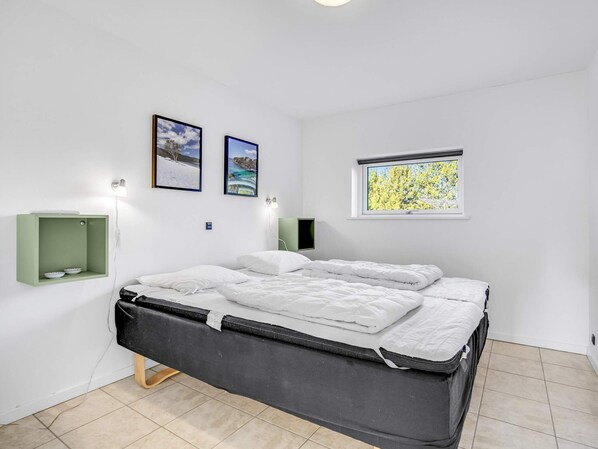 A modern bedroom with a bed, two wall-mounted picture frames, a small shelf with bowls, and a window with a view of trees.