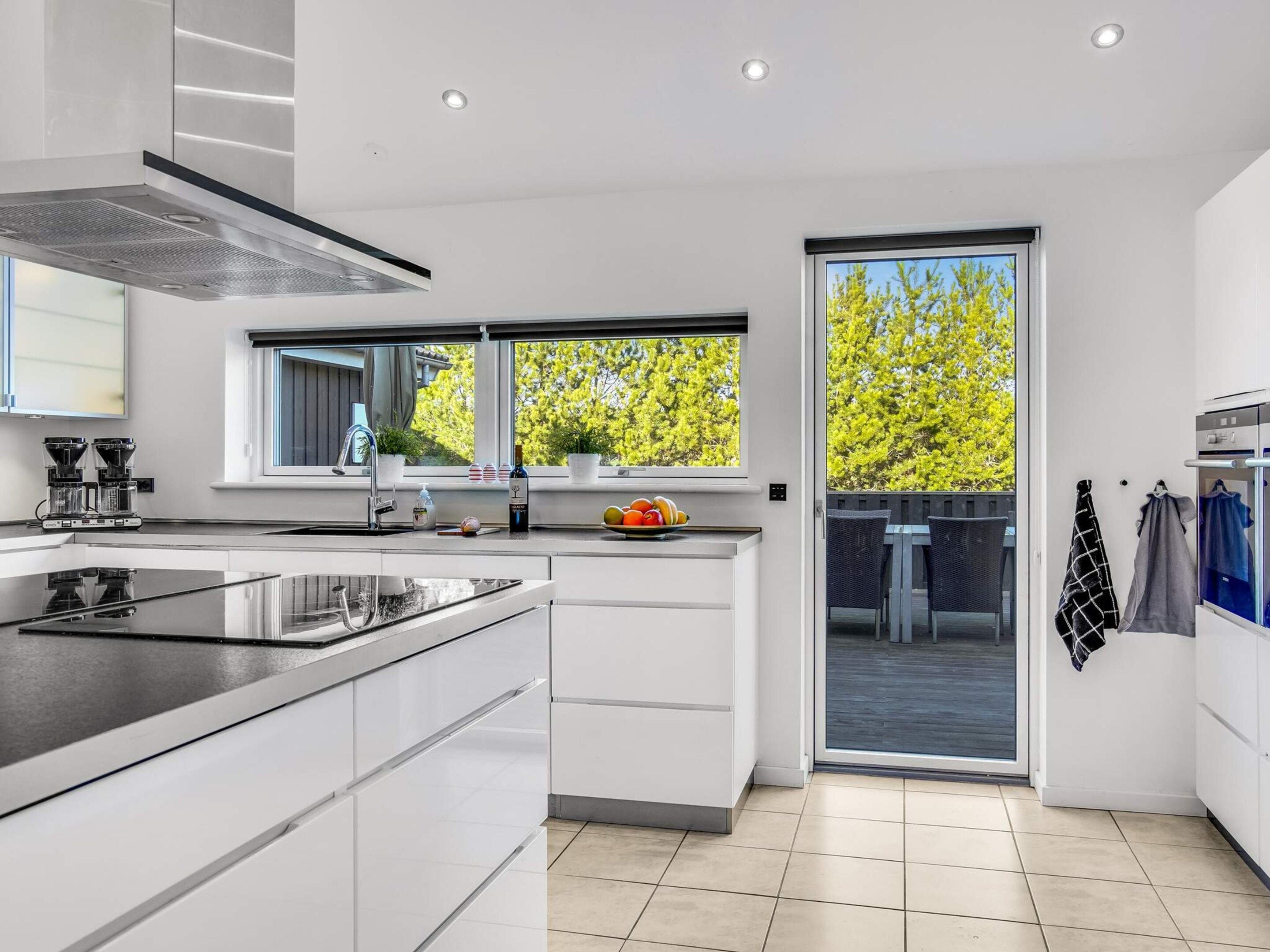 A modern kitchen with a large island, built-in appliances, and a sliding glass door leading to an outdoor area.