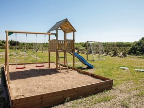 A wooden play structure with a slide, swings, and a climbing ladder. - 5 Star Holiday Home in Jerup (Jerup)