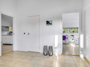 A modern interior with a white door, tiled floor, and a view of a dining area with chairs and a table. - 5 Star Holiday Home in Jerup (Jerup)