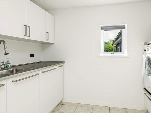 A modern kitchen with white cabinets, a stainless steel sink, a window with a view, and a built-in washing machine.