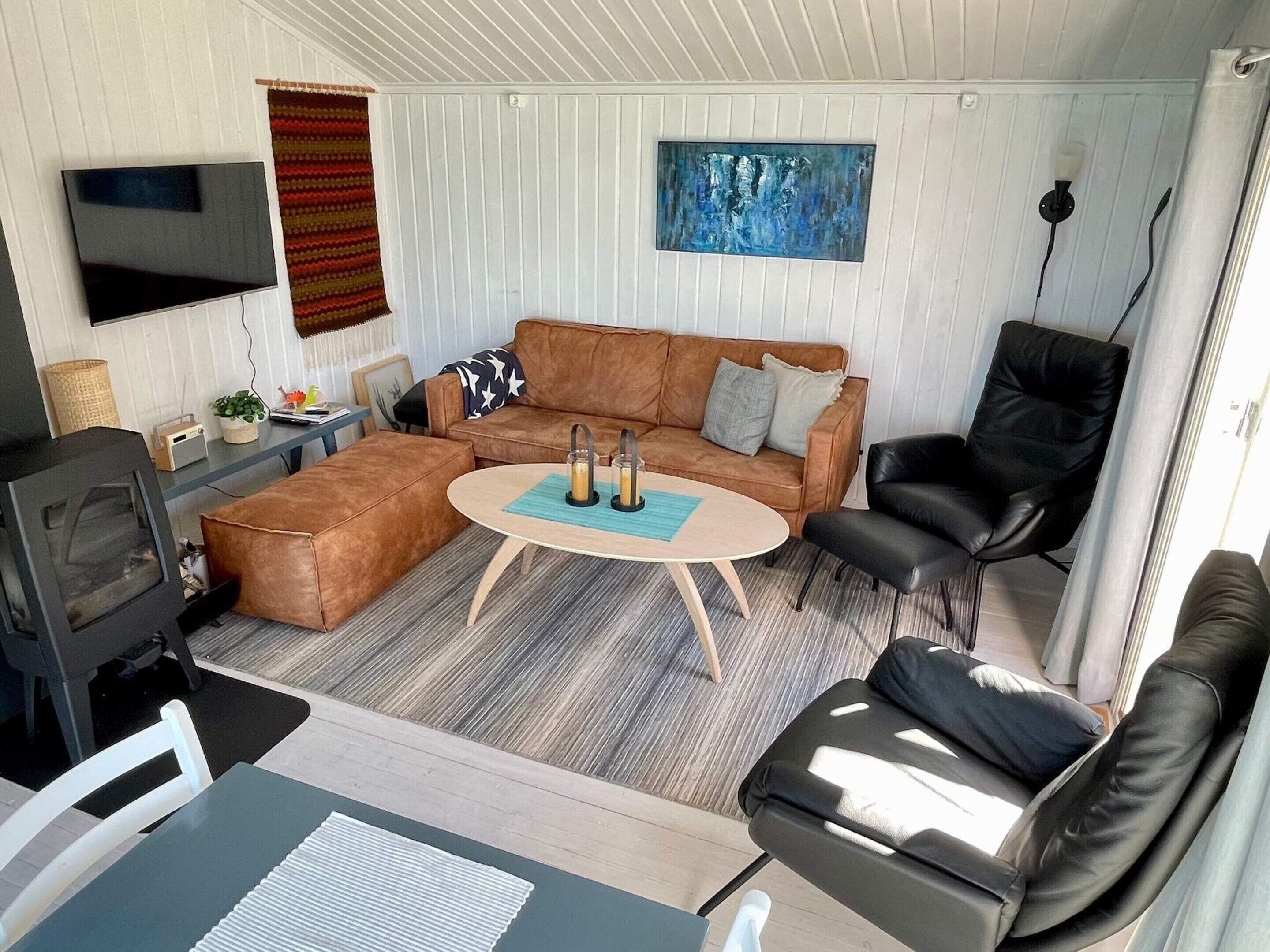 A cozy living room with a brown sectional sofa, a black leather chair, a small round coffee table, a flat-screen TV, and a painting on the wall.