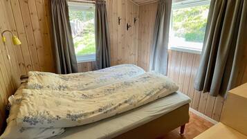 A wooden-paneled room with a bed, two windows with curtains, and a small table.