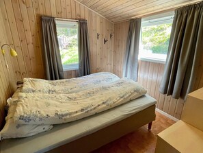 A wooden-paneled room with a bed, two windows with curtains, and a small table. - 6 Person Holiday Home in Etne (Etne)