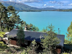A cabin with a metal roof, surrounded by trees and a lake. - 6 Person Holiday Home in Etne (Etne)