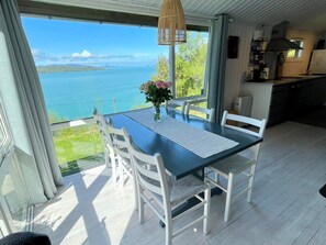 A dining area with a table and chairs, a view of the sea, and a kitchen in the background. - 6 Person Holiday Home in Etne (Etne)