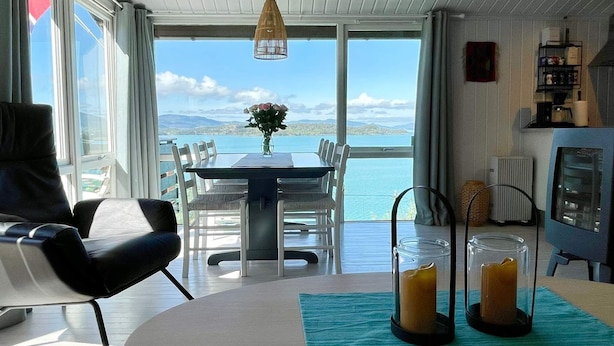 A dining area with a table and chairs, a vase with flowers, and a view of the sea. - 6 Person Holiday Home in Etne (Etne)