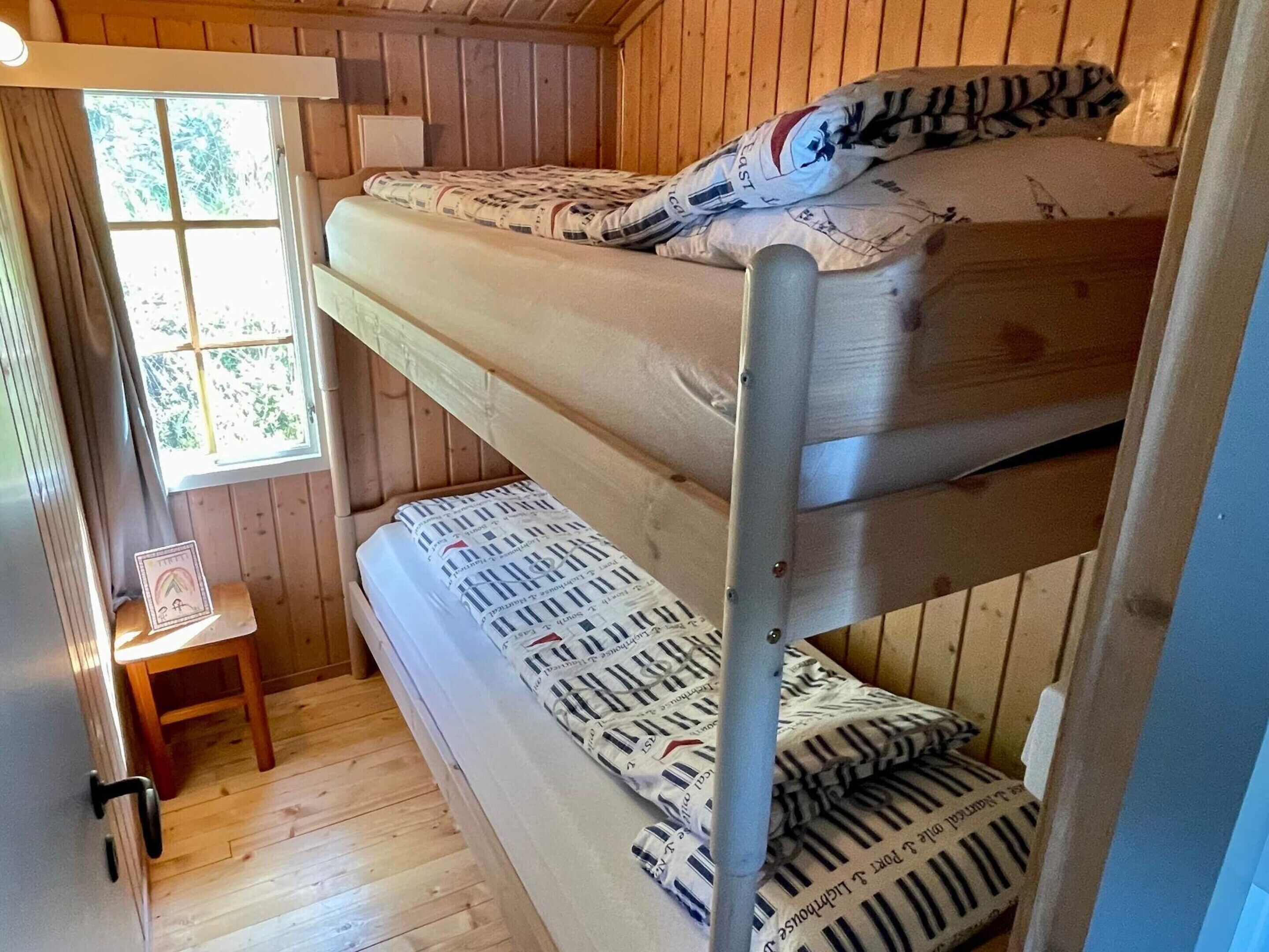 A bunk bed with patterned bedding in a wooden room with a window and a small table.