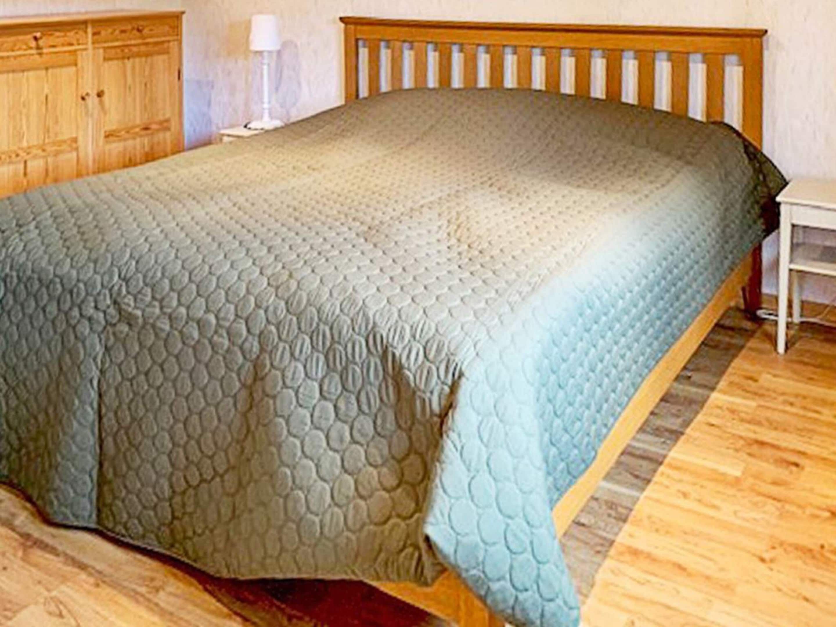 A bedroom with a bed, wooden headboard, and a nightstand with a lamp.