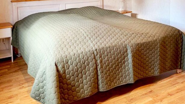 A bed with a quilted cover, a wooden headboard, a bedside table with a lamp, and a wooden floor. - 5 Person Holiday Home in Hagfors (Hagfors)