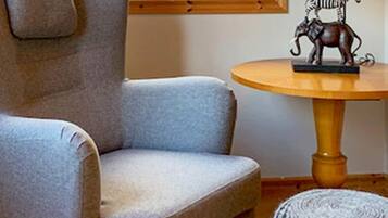 Una habitación con un sillón gris, una mesa redonda de madera y una escultura metálica decorativa, además de una alfombra estampada.