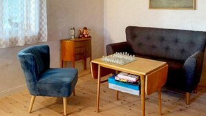 A room with a blue armchair, a sofa, a wooden coffee table with a chess set, a small wooden side table with a clock and a decorative item, and a framed picture on the wall. - 5 Person Holiday Home in Hagfors (Hagfors)
