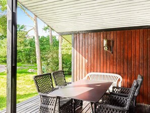 An outdoor patio with a table and chairs, a wooden wall, and a view of greenery. - 6 Person Holiday Home in Vig (Vig)