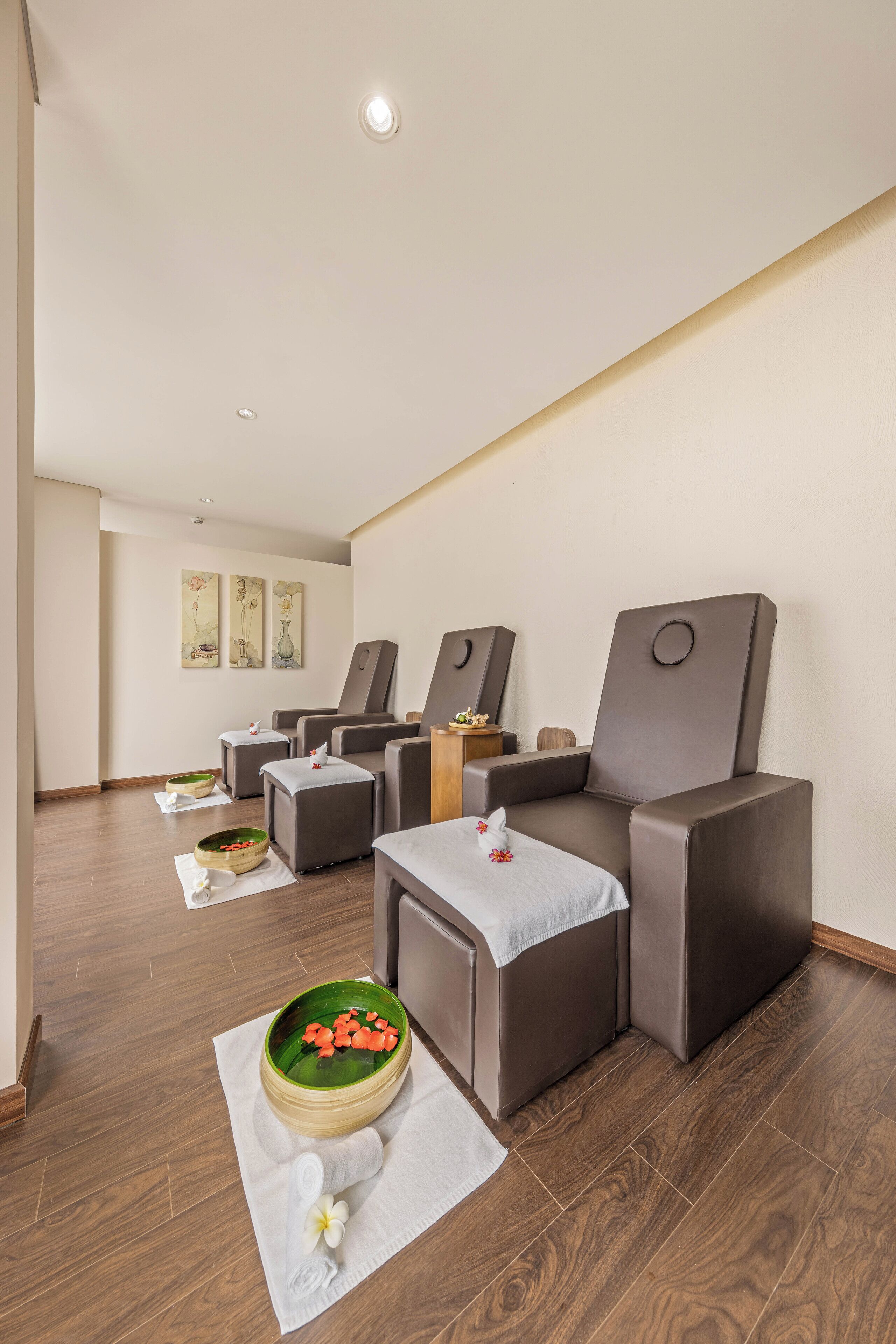 A modern spa room with multiple massage chairs, a small table with a bowl of flowers, and a wooden floor.
