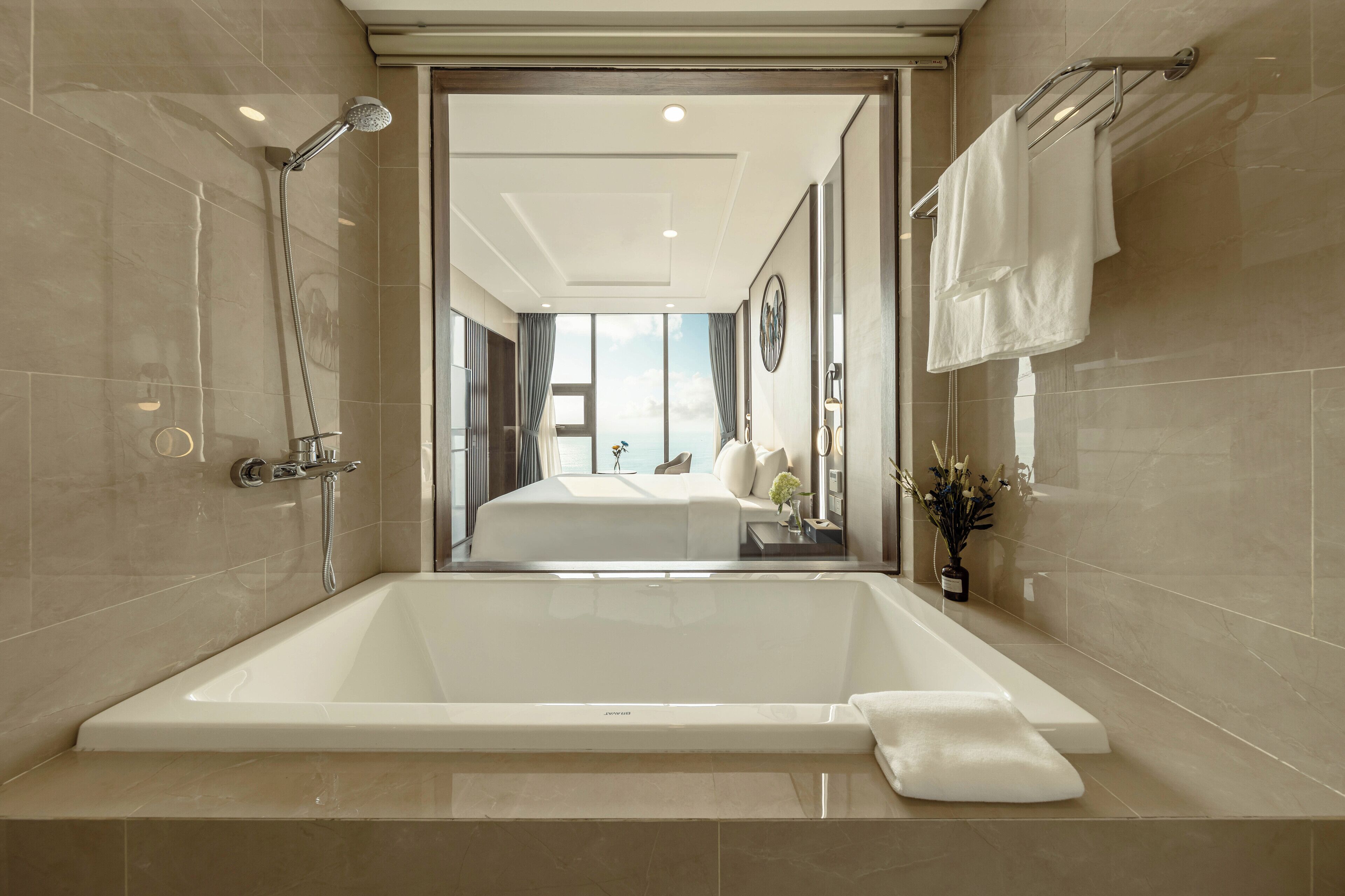 A modern bathroom with a large bathtub, a shower, and a view into the bedroom.