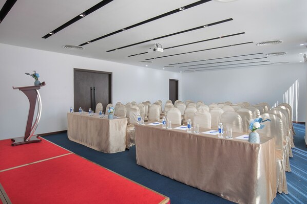 A conference room with a long table, rows of chairs, a podium, and a red carpet. - Mangata Beachfront Hotel (Da Nang)