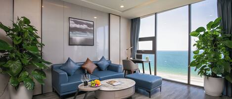 A modern living room with a blue sofa, a round coffee table, and large windows offering a view of the beach.