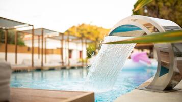Ein Pool mit Wasserspiel, einer Holzterrasse und einem überdachten Sitzbereich.