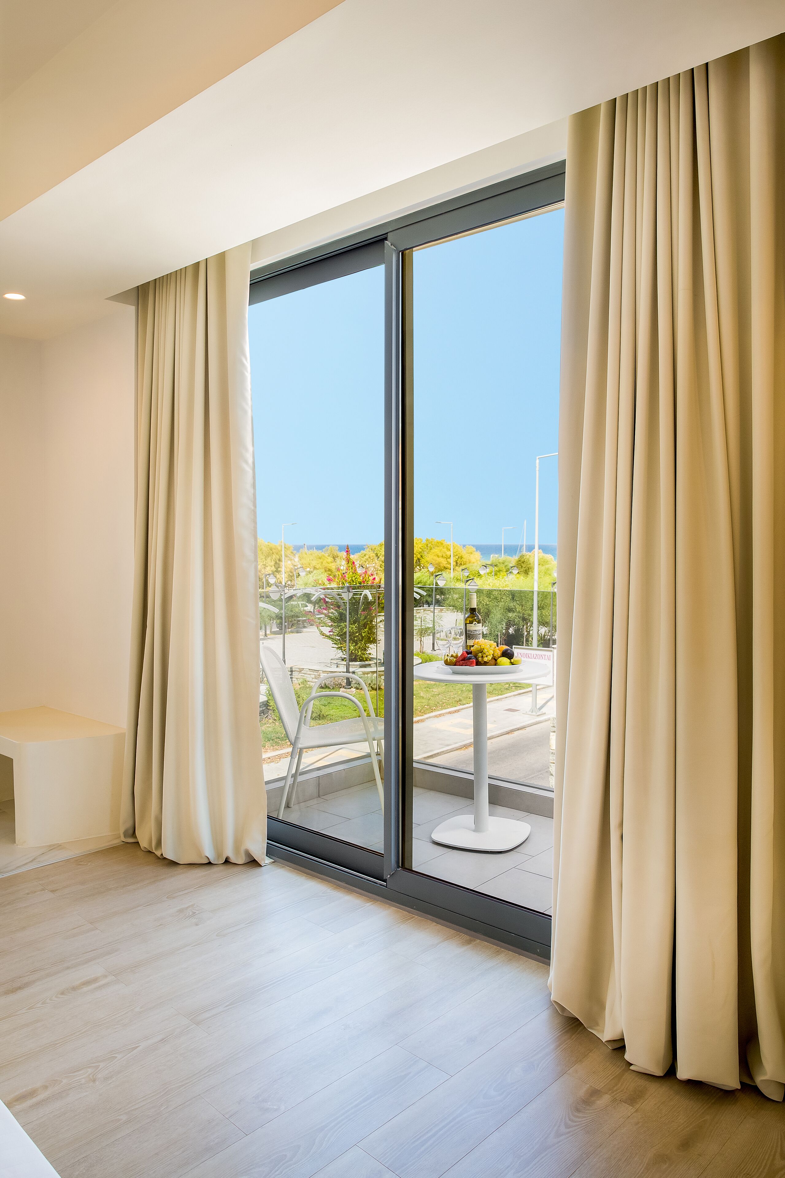 A modern room with a large sliding glass door leading to a balcony with a table of fruit and a bottle of wine.