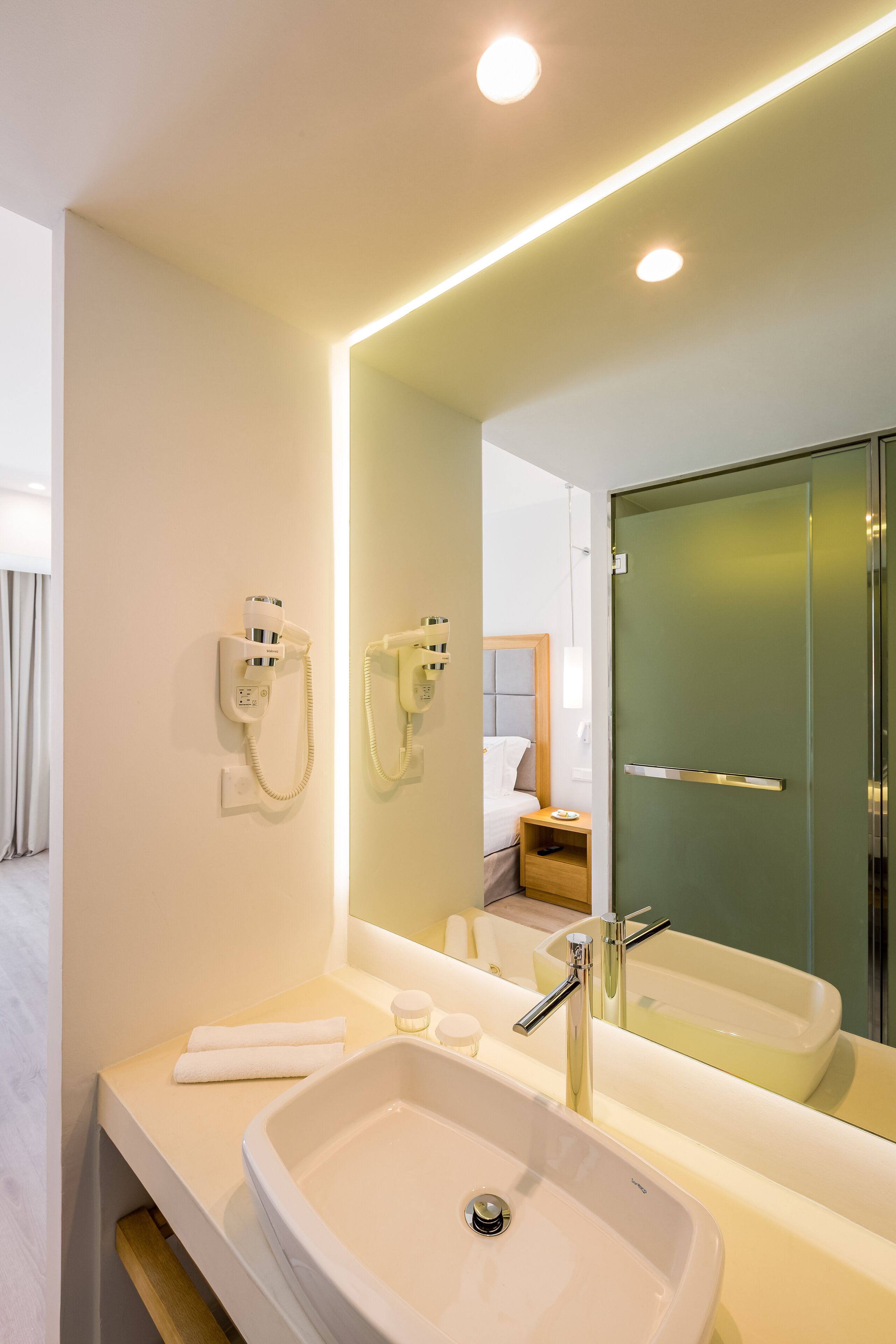 Un baño moderno con un lavamanos grande, un espejo y un secador de pelo montado en la pared.