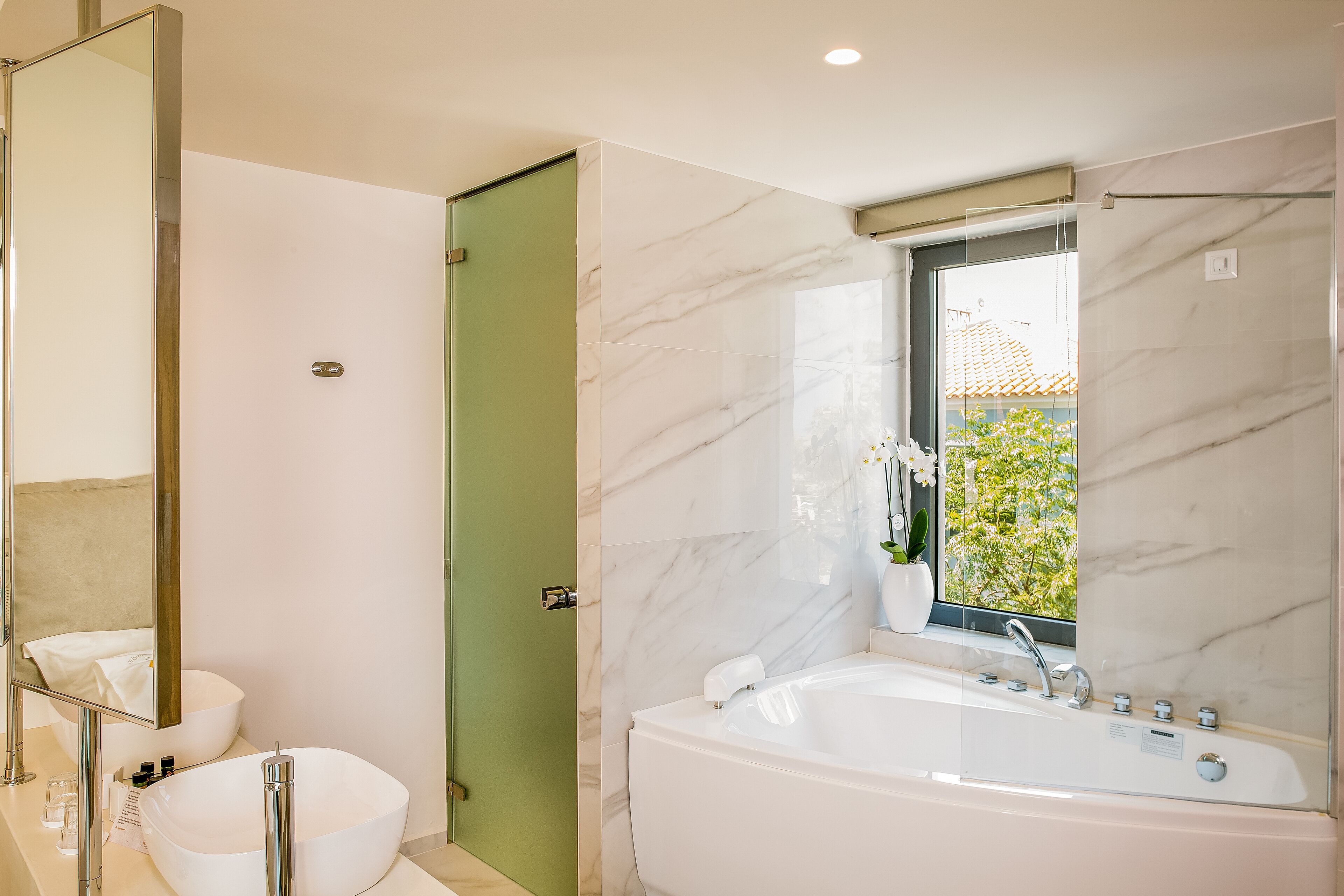 Un baño moderno con una bañera grande, un lavabo redondo y una puerta verde.