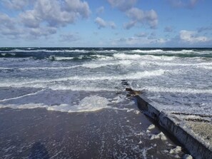 A beach with waves crashing onto the shore and a concrete barrier in the foreground. - 6 Person Holiday Home in Vejby (Vejby)