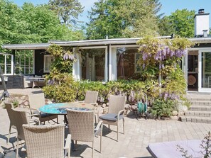 An outdoor patio area with wicker furniture, a table, and a pergola covered with purple flowers. - 6 Person Holiday Home in Vejby (Vejby)