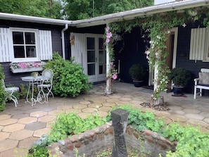 A house with a patio area, a white outdoor table and chairs, and a variety of potted plants.