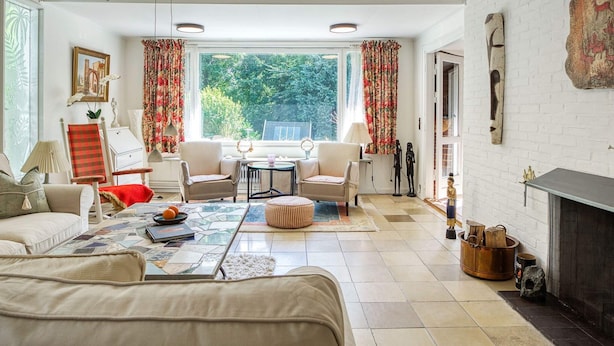 A spacious living room with a fireplace, a large window with curtains, and a view of greenery outside.