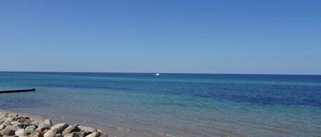 A rocky shoreline with clear blue water and a distant boat.