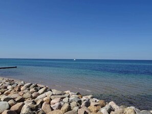 A rocky shoreline with clear blue water and a distant boat. - 6 Person Holiday Home in Vejby (Vejby)