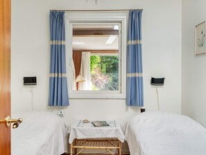 Een kamer met twee bedden, een raam met gordijnen, een nachtkastje en een lamp.