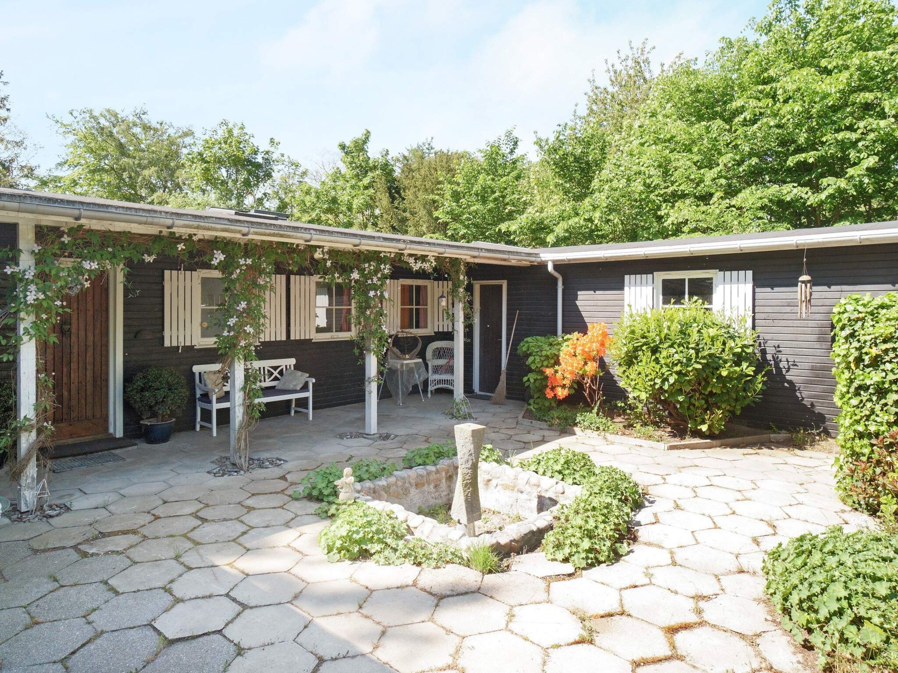 A house with a covered patio area, a stone pathway, and a small garden with various plants.