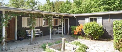 A house with a covered patio area, a stone pathway, and a small garden with various plants.