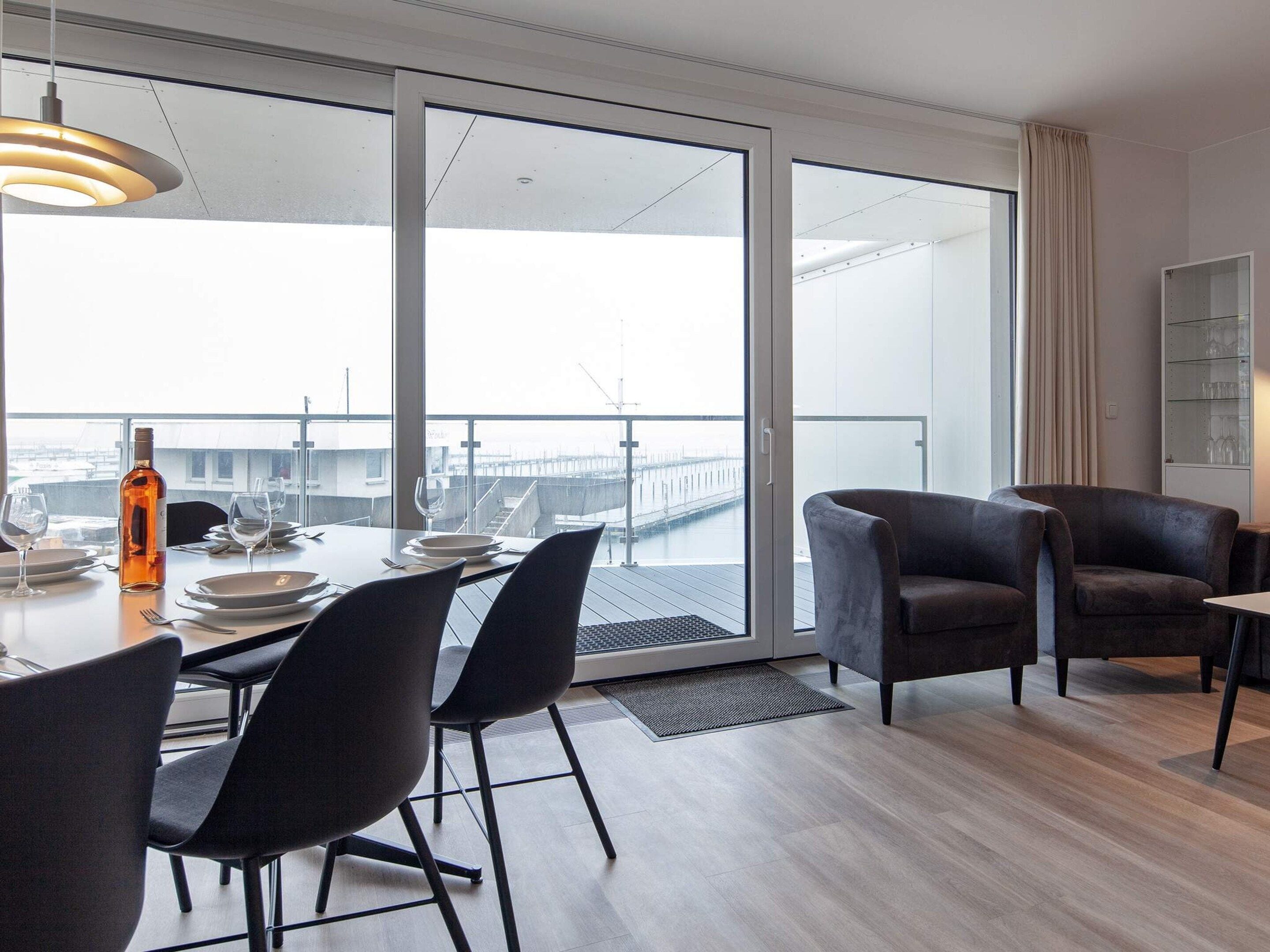 Un espace de restauration moderne avec une table dressée pour deux personnes, une bouteille de vin et une vue sur un quai, visible à travers de grandes portes-fenêtres coulissantes.