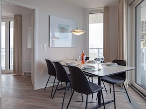 A modern dining area with a table set for four, black chairs, a pendant light, and a bottle of wine.