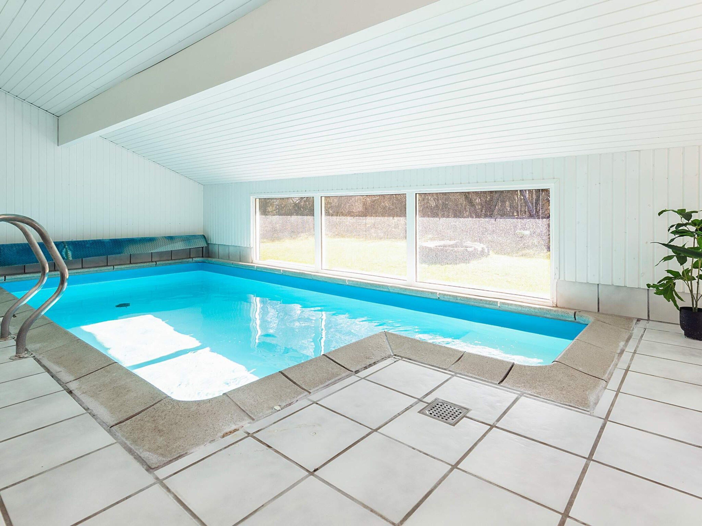 An indoor swimming pool with a clear view outside, a tiled floor, and a metal pool ladder.