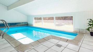 An indoor swimming pool with a clear view outside, a tiled floor, and a metal pool ladder.