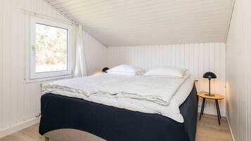 A bedroom with a bed, a window, a bedside table with a lamp, and a wooden floor.