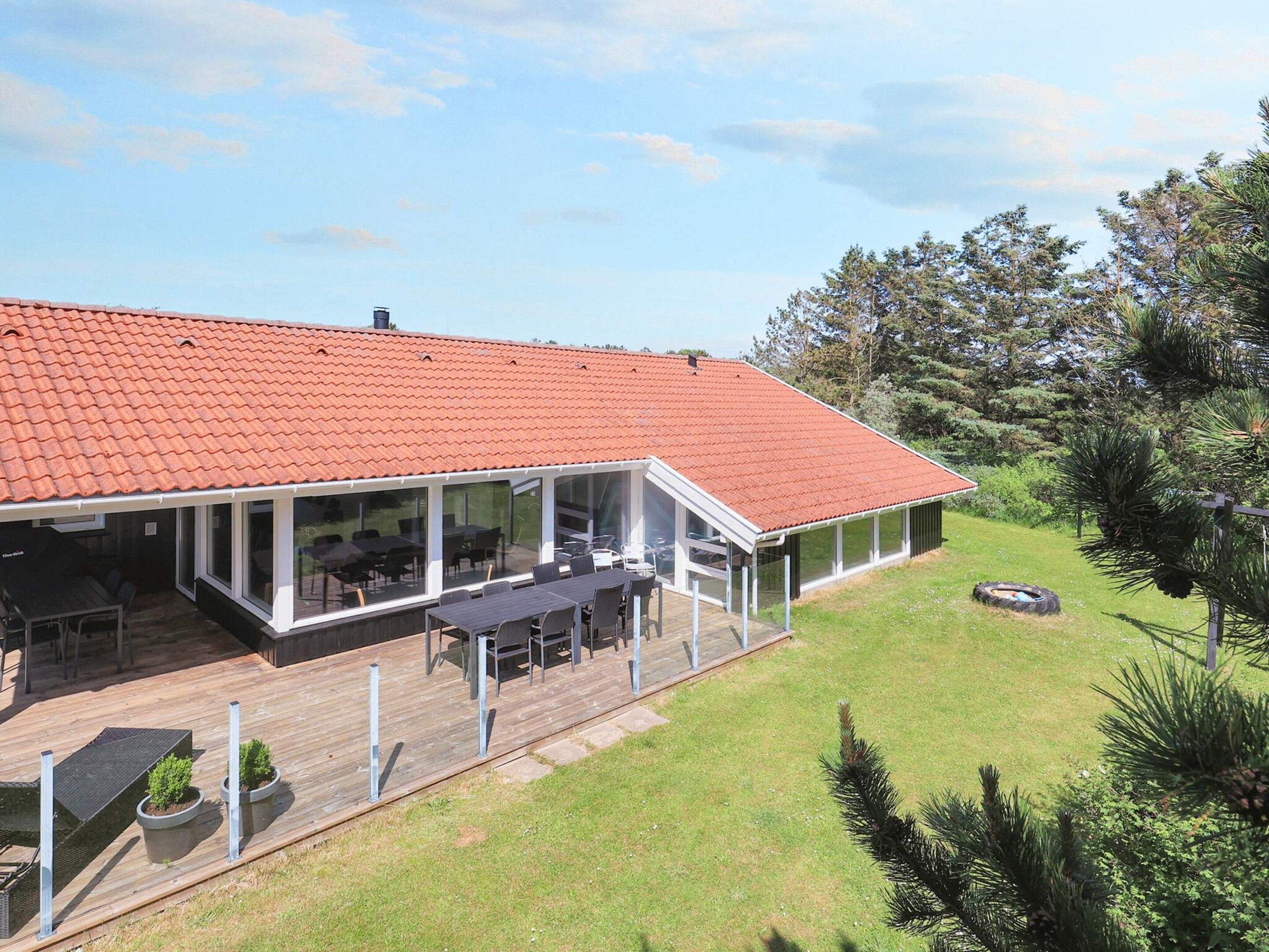 A house with a red tiled roof, a covered patio with outdoor furniture, and a grassy yard.