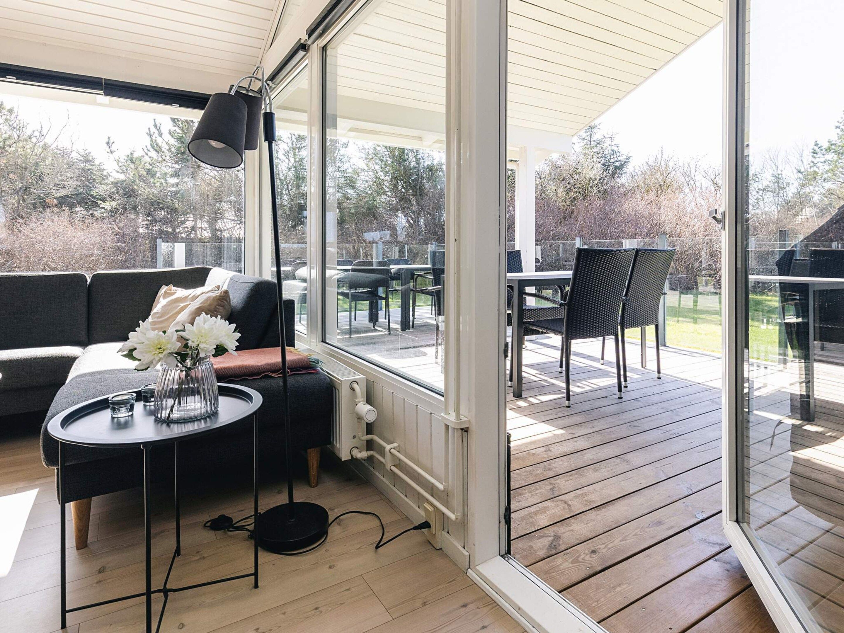 A modern outdoor seating area with a sofa, a round table, and a floor lamp, overlooking a wooden deck and garden.